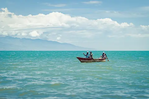 Fiskare i en träbåt på turkost vatten i Tanganyikasjön vid Bujumbura, med berg i bakgrunden