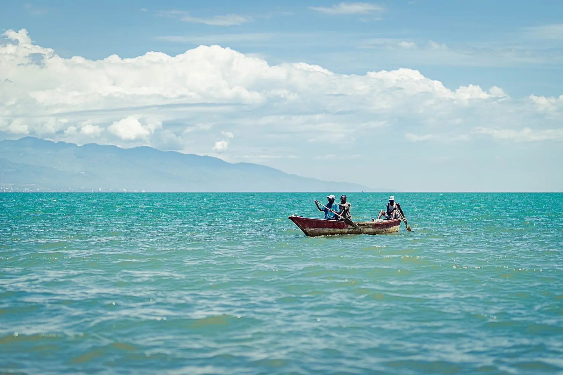 Fiskare i en träbåt på turkost vatten i Tanganyikasjön vid Bujumbura, med berg i bakgrunden