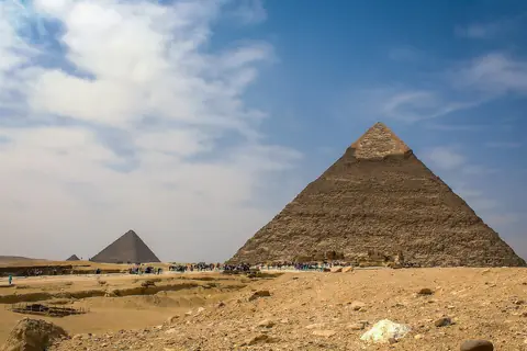Två av pyramiderna i Giza i ökensand under blå himmel med drivande moln