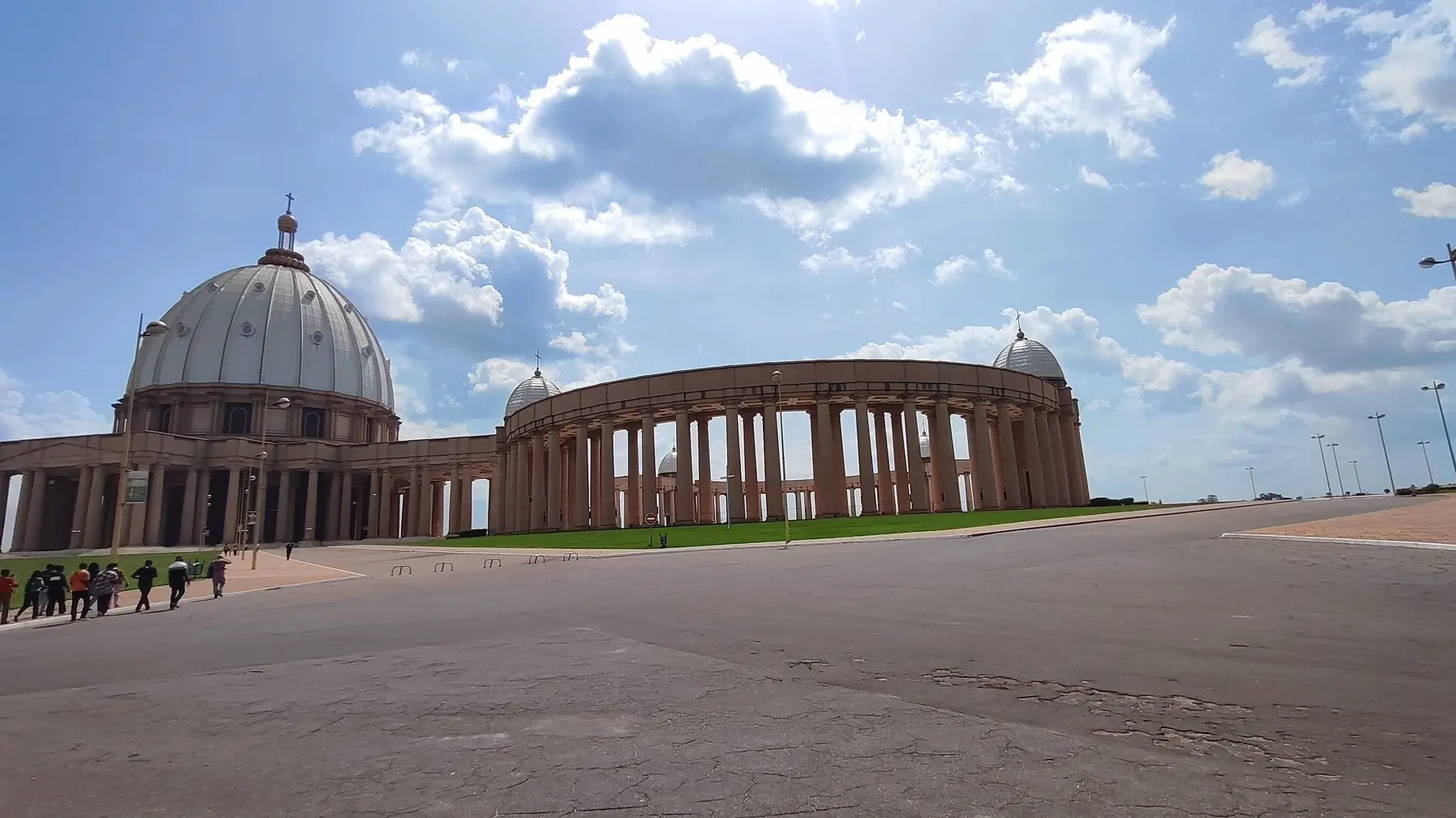Basilikan Notre-Dame de la Paix i Yamoussoukro med stor kupol och pelargångar under blå himmel med vita moln