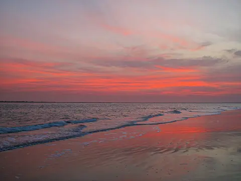 Rosa och orange himmel som speglas i vågorna vid stranden i Banjul i gryningen