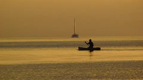 Silhuett av en man i en kanot och en segelbåt på Malawisjön i gyllene kvällsljus