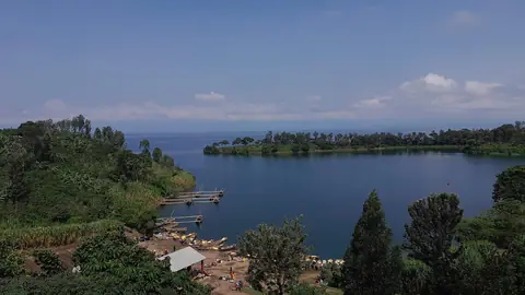 Blå vik i Kivusjön omgiven av gröna kullar och båtbryggor i västra Rwanda