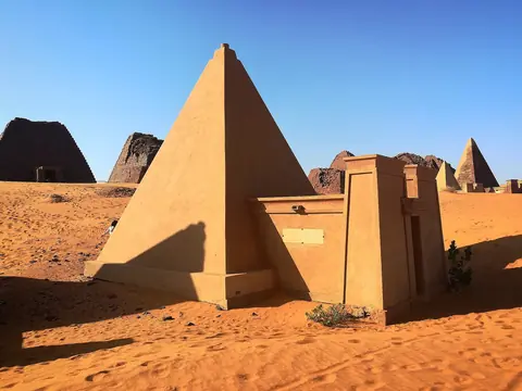 Branta sandstenspyramider i orange ökensand under blå himmel vid Meroe