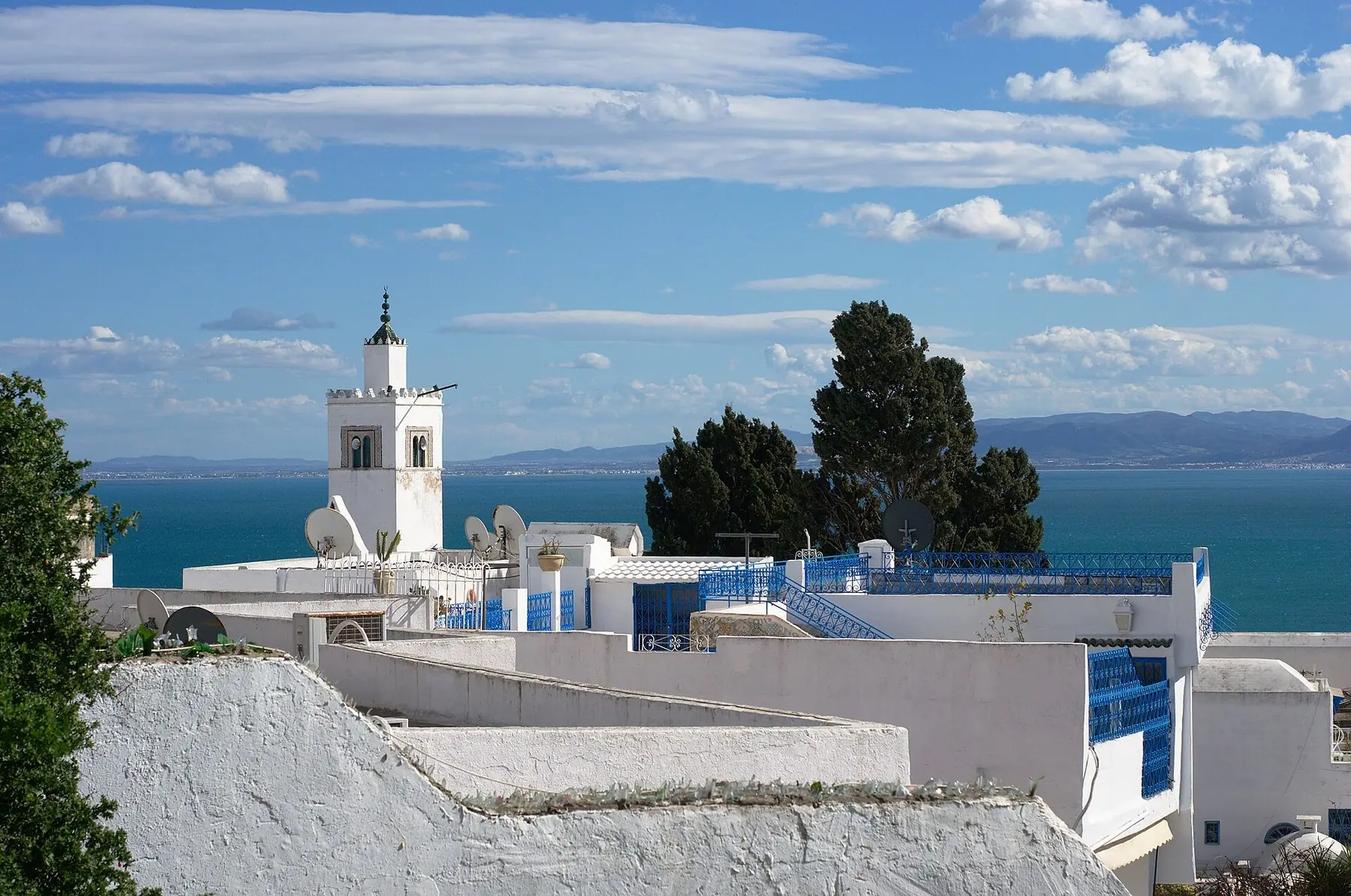 Vita hus med blå detaljer och en minaret ovanför det blå havet i Sidi Bou Said