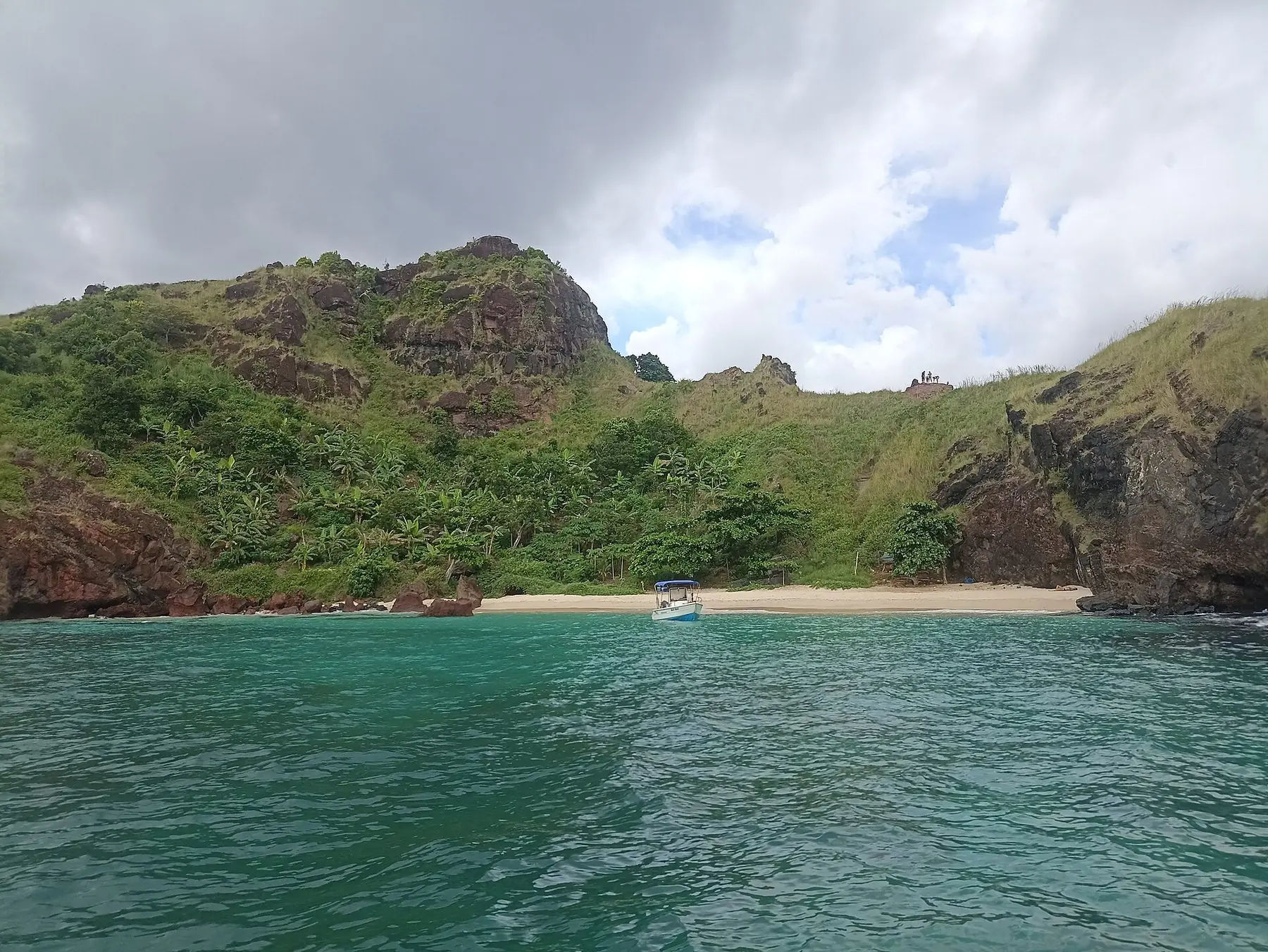 Liten sandstrand under gröna klippiga kullar vid det turkosa vattnet på holmen Malandzamiayatsini vid Mayotte