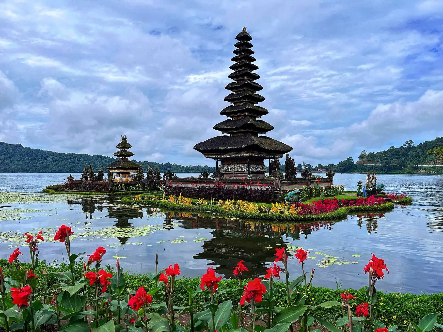 Templet Pura Ulun Danu Bratan med sina höga pagodtak i sjön Bratan på Bali, med röda blommor i förgrunden