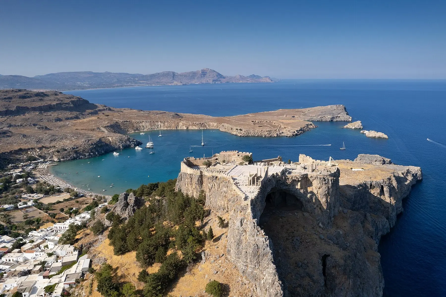Akropolis i Lindos på en klippa ovanför turkosa vikar och segelbåtar på Rhodos, sett från luften