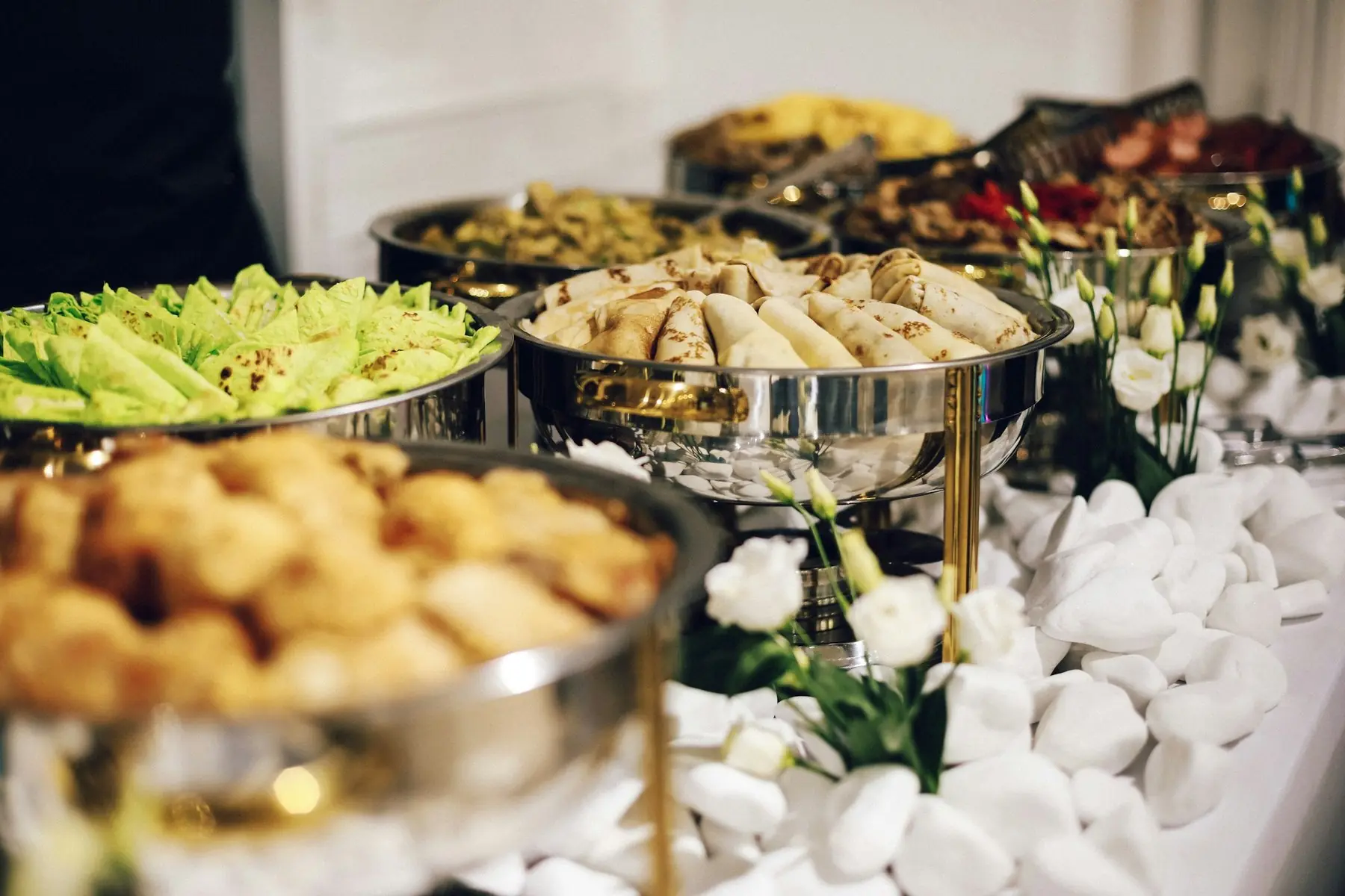 Buffé med varmrätter och sallader i blanka serveringskärl, dekorerad med vita blommor