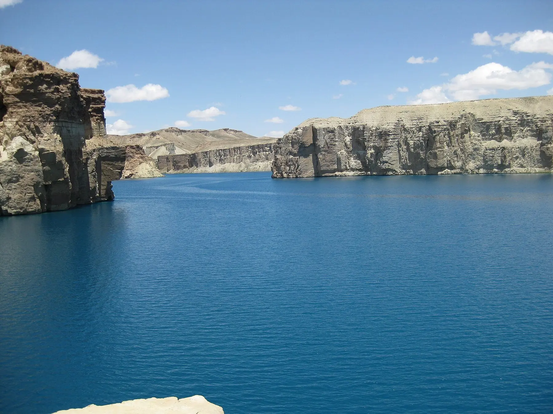 Djupblå sjö mellan höga kalkstensklippor under blå himmel i nationalparken Band-e Amir