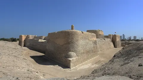 Den gamla sandstensfästningen Qal'at al-Bahrain under klarblå himmel med höghus i fjärran