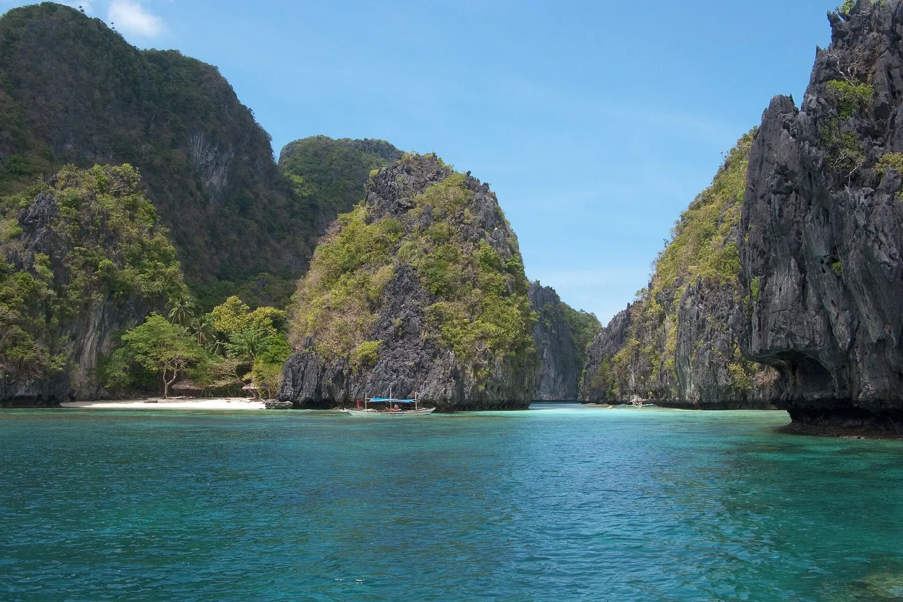 Branta kalkstensklippor med grönska kring en turkos vik i Bacuitbukten vid El Nido på Palawan