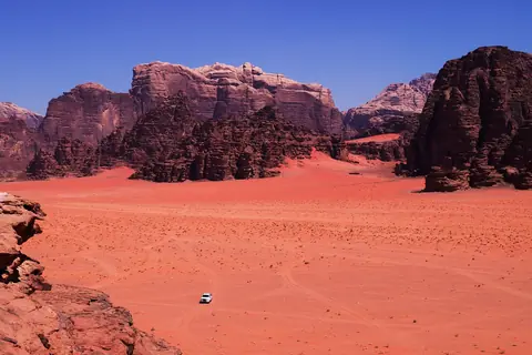Röd sandöken mellan höga sandstensberg i Wadi Rum i Jordanien, sedd ovanifrån med en ensam terrängbil