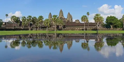Angkor Wats tempeltorn och palmer som speglar sig i en stilla damm under blå himmel