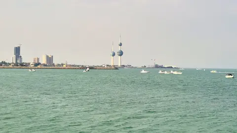 Kuwait Towers med sina klotformade torn vid kusten sedda från det gröna havet med småbåtar