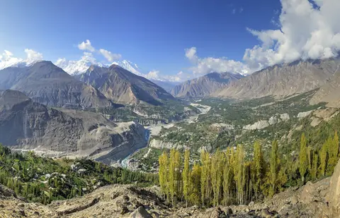 Hunzadalen med höstgula popplar, en slingrande flod och höga bergstoppar under blå himmel i norra Pakistan