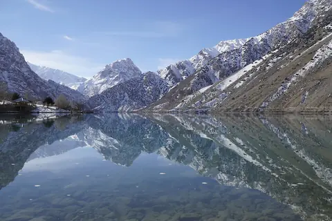Snöklädda bergstoppar speglar sig i den stilla bergsjön Iskanderkul i Fanbergen i Tadzjikistan