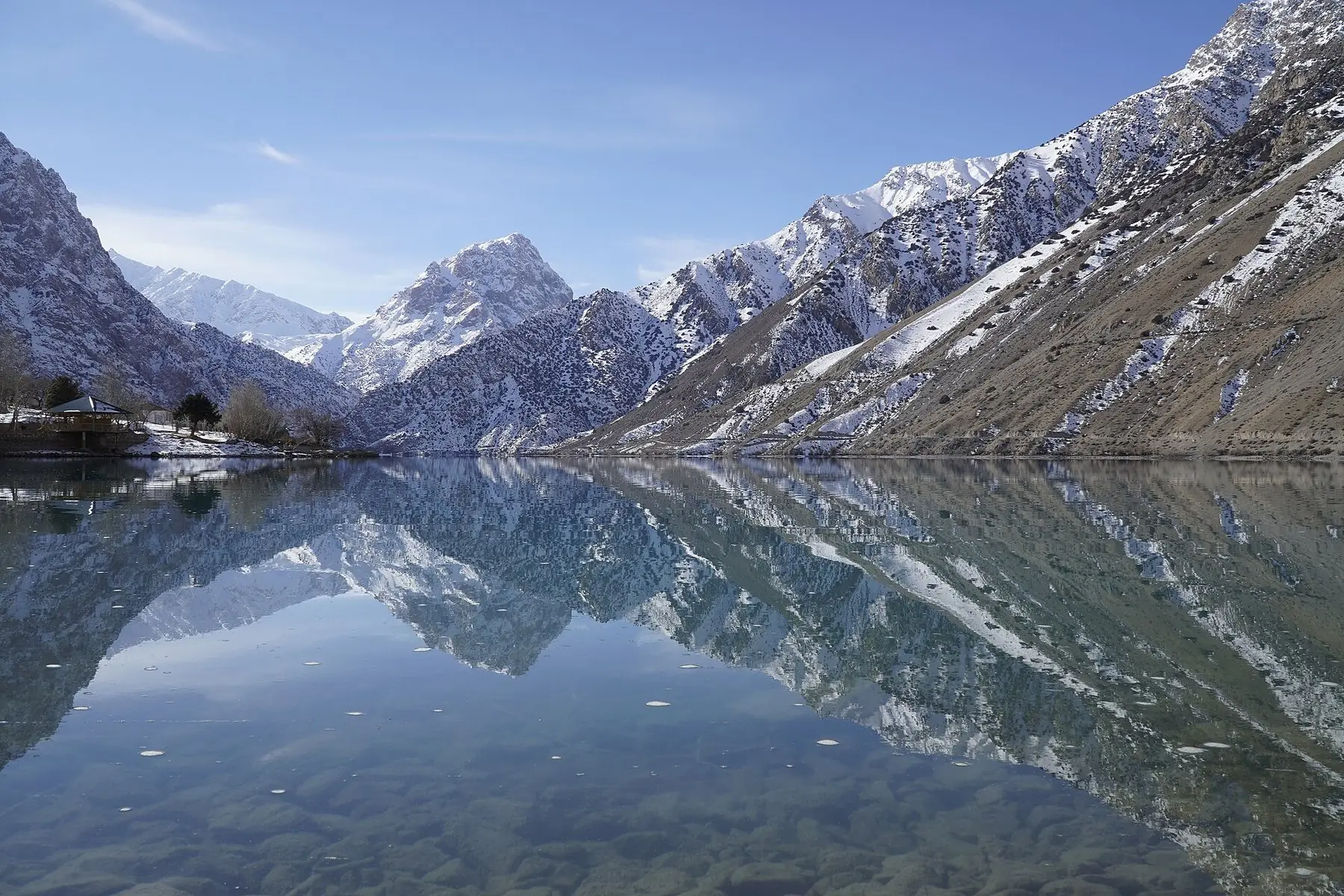 Snöklädda bergstoppar speglar sig i den stilla bergsjön Iskanderkul i Fanbergen i Tadzjikistan