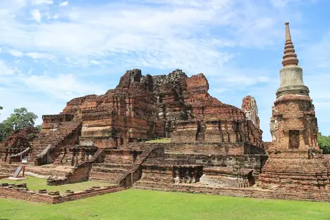 Ruiner av tegeltempel och en vit stupa på gräsmatta i Wat Mahathat i Ayutthaya