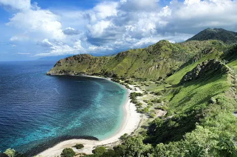 Vit sandstrand i en turkos vik under gröna kullar vid Areia Branca utanför Dili i Östtimor