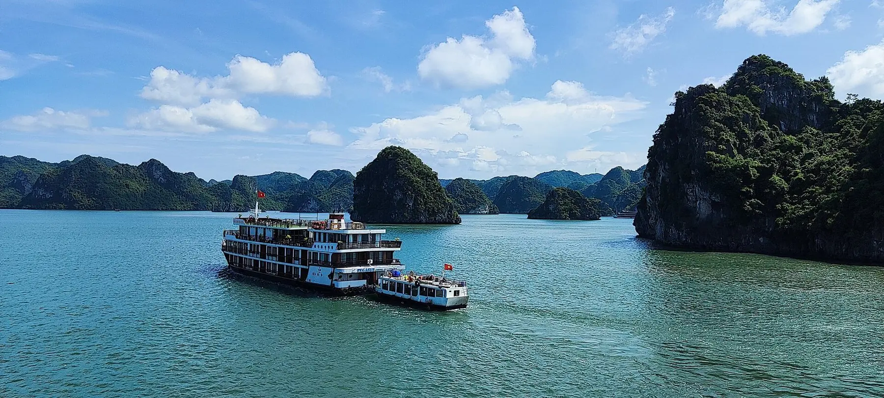 Kryssningsbåtar bland skogklädda kalkstensöar i det turkosa vattnet i Ha Long-bukten