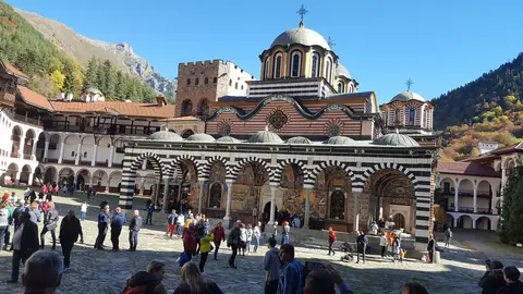 Rilaklostrets randiga kyrka med kupoler på gården, omgiven av klosterbyggnader och skogsklädda berg
