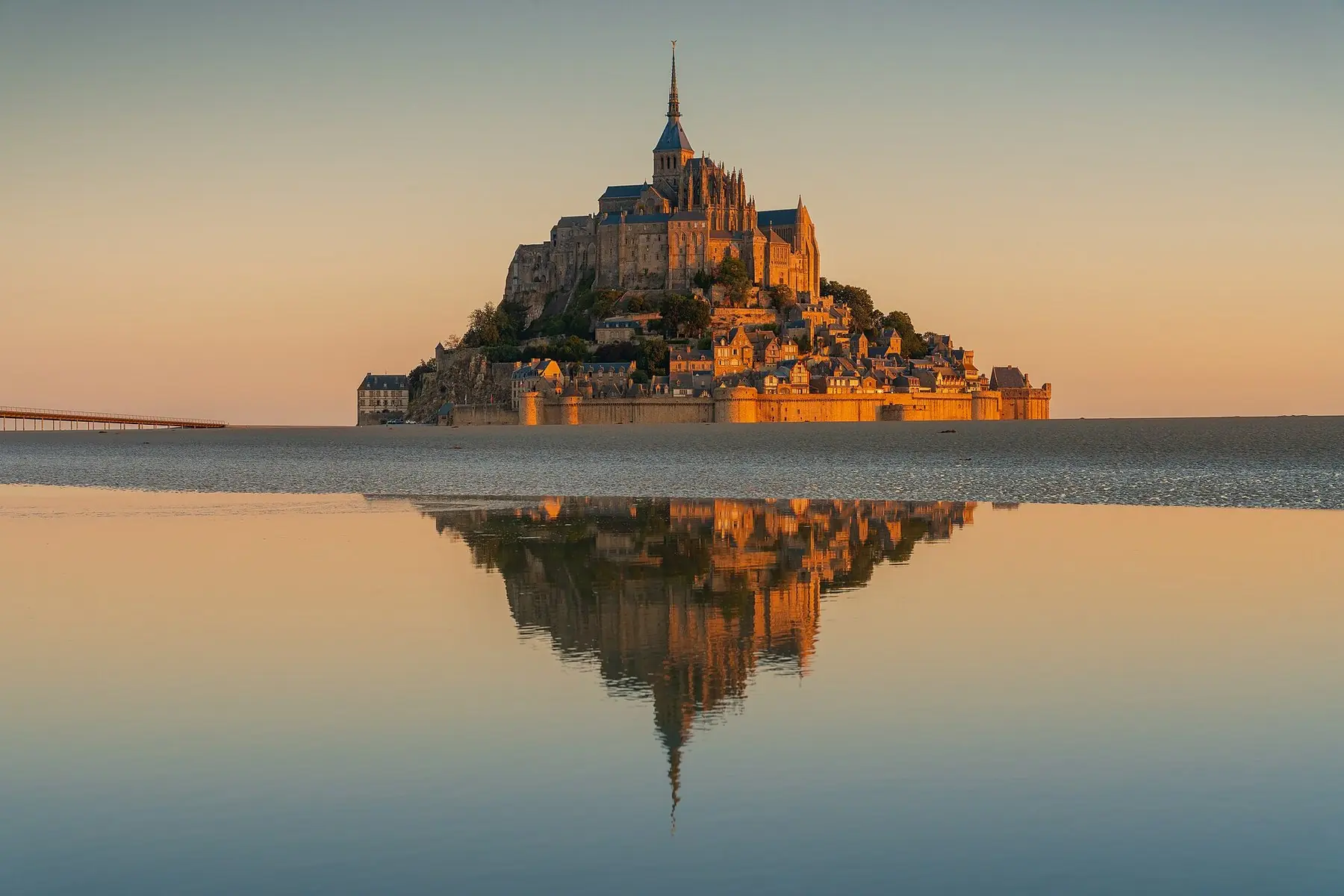 Klosterön Mont-Saint-Michel i soluppgångens gyllene ljus, speglad i det blanka vattnet
