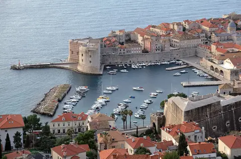 Dubrovniks gamla hamn med småbåtar, fästningsmurar och röda tegeltak mot Adriatiska havet