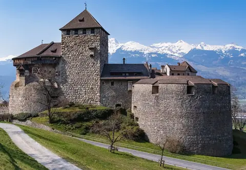 Slottet i Vaduz med stentorn och runda murar framför snöklädda alptoppar i Liechtenstein