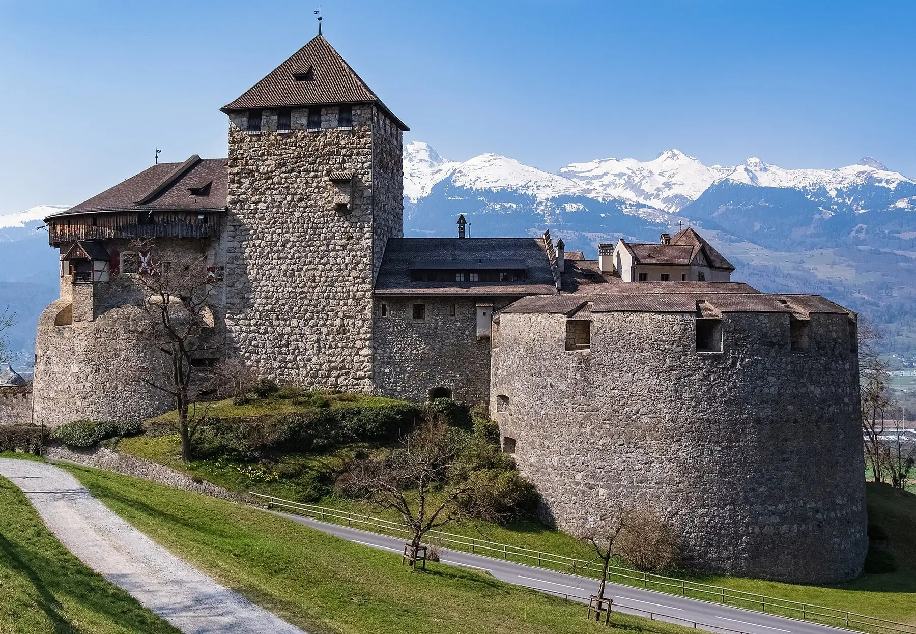 Slottet i Vaduz med stentorn och runda murar framför snöklädda alptoppar i Liechtenstein