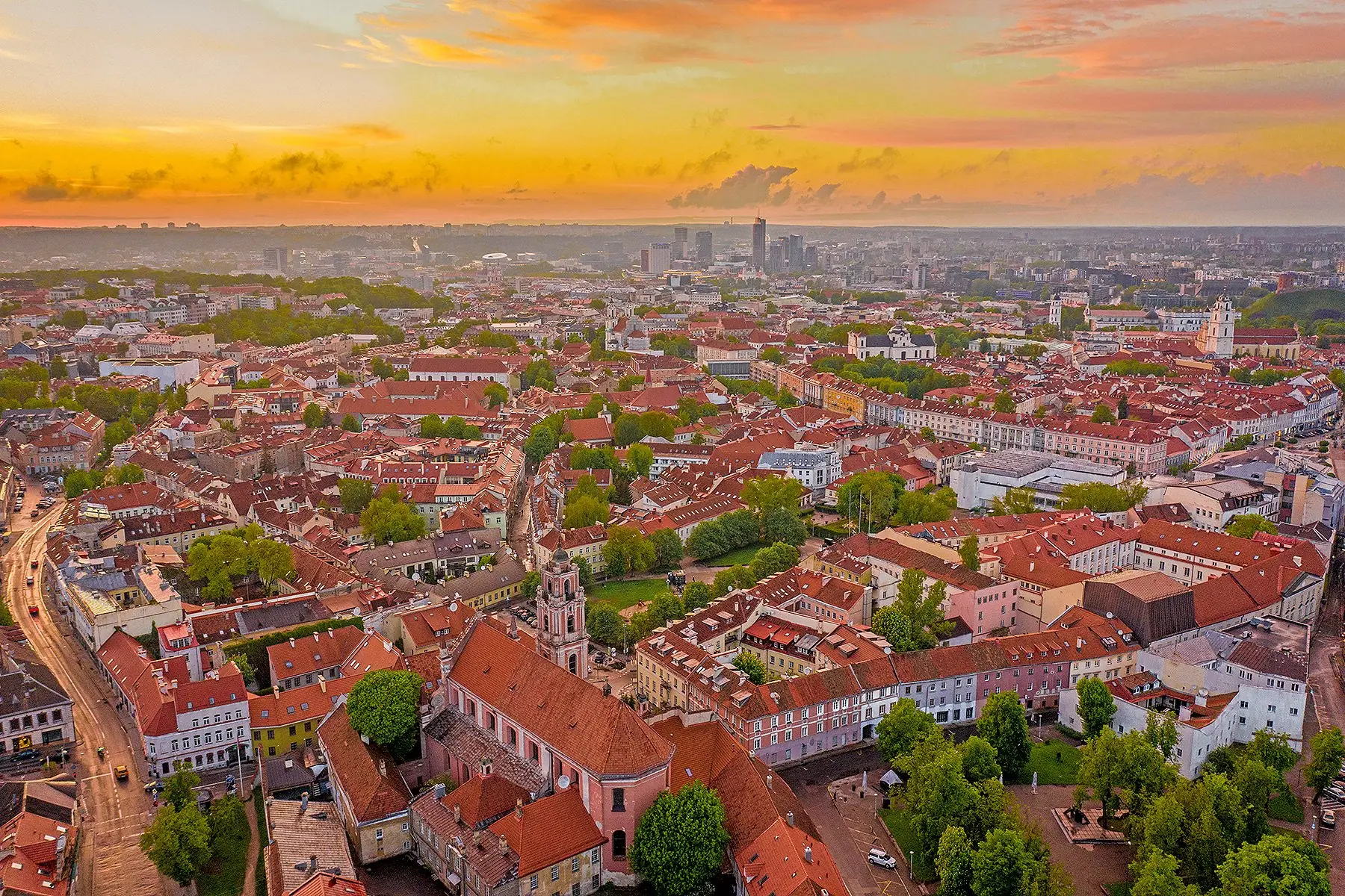 Vilnius gamla stad med röda tegeltak och kyrktorn under en guldfärgad solnedgångshimmel