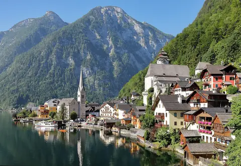 Hallstatts trähus och kyrktorn vid sjön Hallstätter See under branta alptoppar
