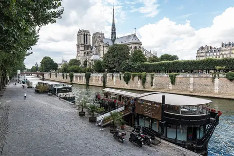 Notre-Dame de Paris bakom träden på Île de la Cité, med husbåtar längs kajen vid Seine