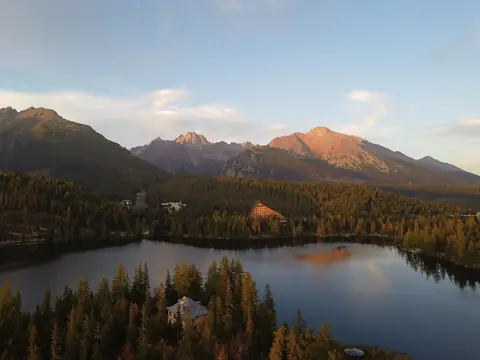Bergsjön Štrbské pleso omgiven av barrskog med Höga Tatras toppar i kvällsljus