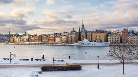 Gamla stans färgglada hus och kyrktorn vid vattnet sedda över en snötäckt kaj i Stockholm