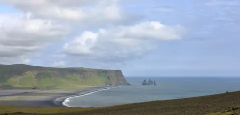 Svart sandstrand och basaltstaplar i havet vid Reynisfjara på Islands sydkust sett från Dyrhólaey