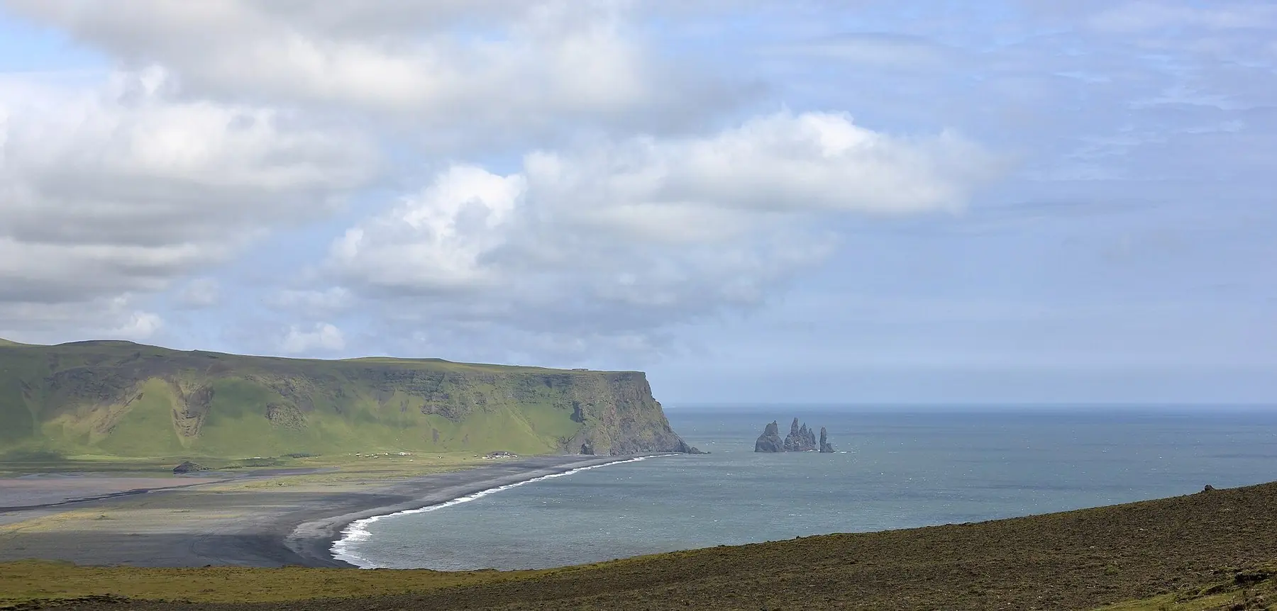 Svart sandstrand och basaltstaplar i havet vid Reynisfjara på Islands sydkust sett från Dyrhólaey