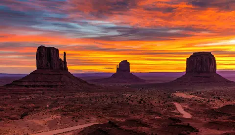 Klippformationerna i Monument Valley i siluett mot en eldröd solnedgång