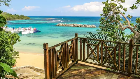 Utsiktsdäck av trä ovanför stranden vid Dunn's River Falls med turkost hav och båtar