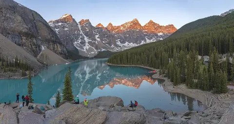 Turkosa Moraine Lake i Banff med skogklädda stränder och bergstoppar i rosa morgonljus