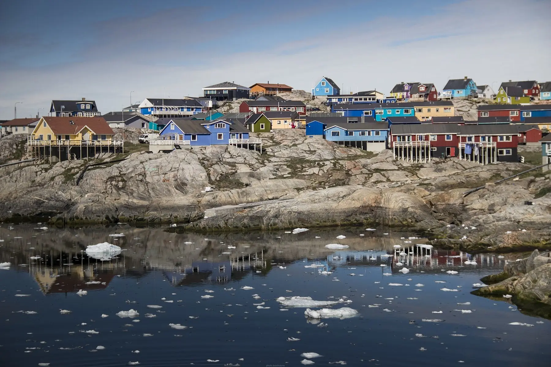 Färgglada trähus på en klippa ovanför vatten med drivande isflak i Ilulissat på Grönland