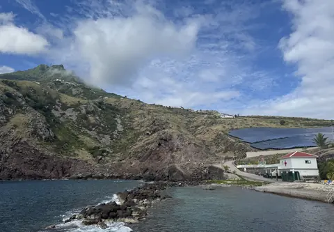 Cove Bay på Saba med branta gröna sluttningar, en vågbrytare och vita hus