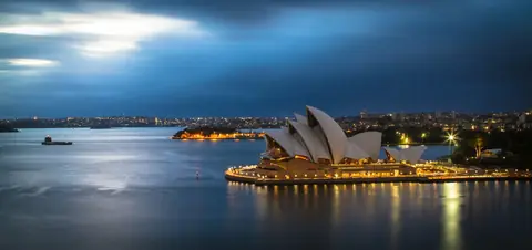 Operahuset i Sydney upplyst i kvällsljus vid hamnen