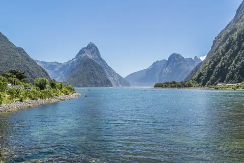 Fjorden Milford Sound med den spetsiga Mitre Peak och branta gröna fjällsidor under klarblå himmel