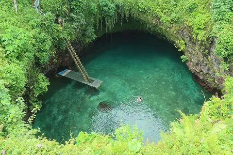 Det turkosa naturbadet To Sua Ocean Trench omgivet av frodig grönska, med en lång trästege ner till vattnet