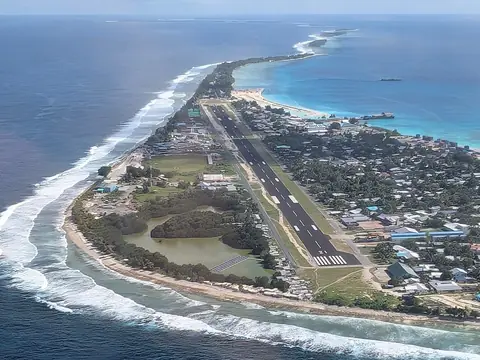 Den smala atollön Fongafale i Funafuti med landningsbana och hus mellan turkos lagun och vita bränningar, sett från luften