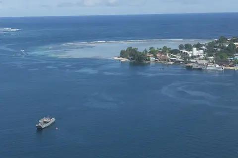 Staden Gizo på en grön udde med korallrev i det djupblå havet och ett vitt fartyg på redden, sett från luften