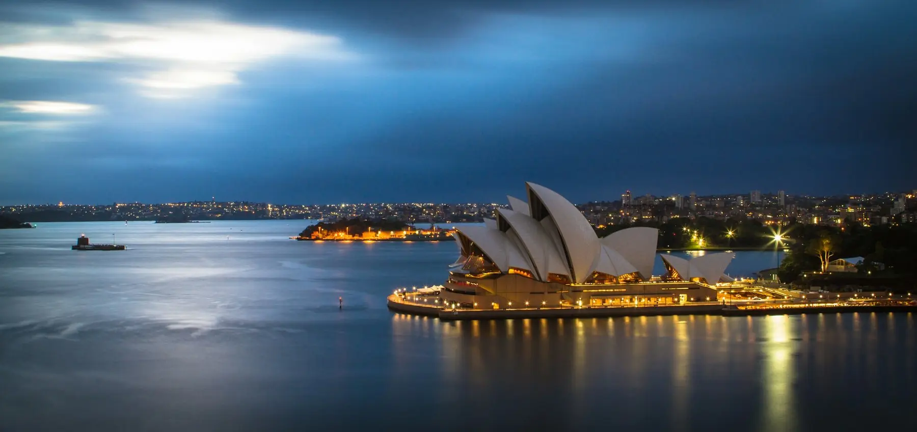 Operahuset i Sydney upplyst i kvällsljus vid hamnen