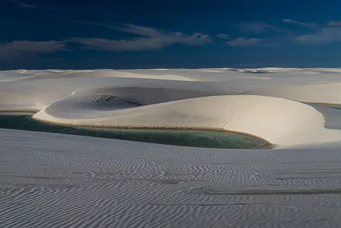 Vita sanddyner och en grön lagun i nationalparken Lençóis Maranhenses